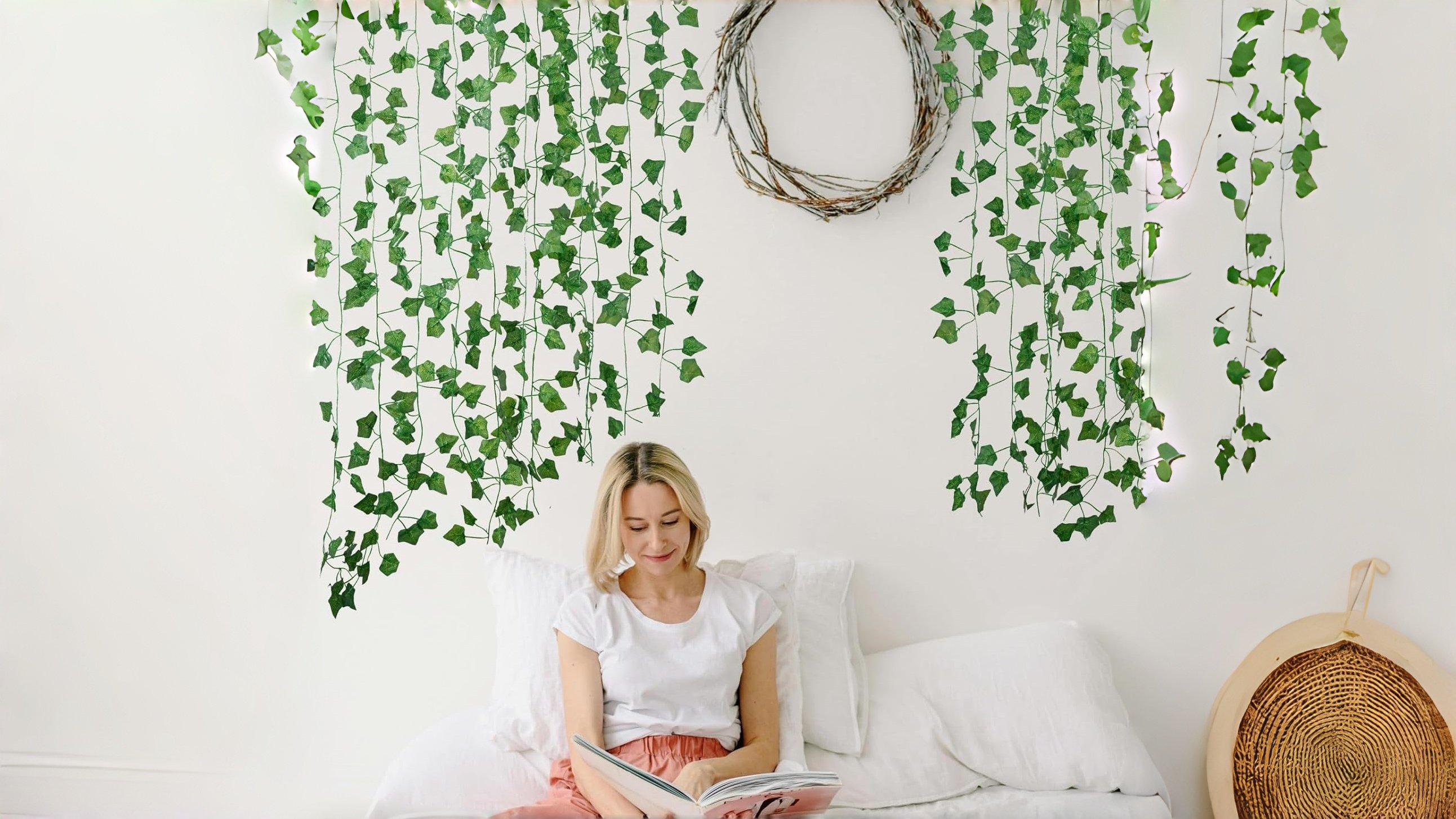 Fake Ivy Vines Above the Headboard - Bedroom Wall Greenery Decor Woman reading in bed with artificial ivy vines hanging above the headboard alongside a twig wreath and string lights
